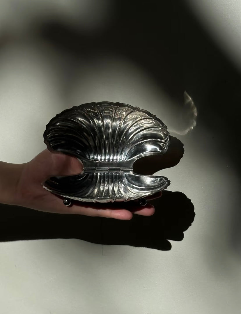Silver shell-shaped object held by a hand on a light background