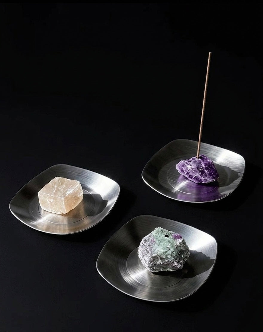 Three metallic incense holders with crystals on a black background