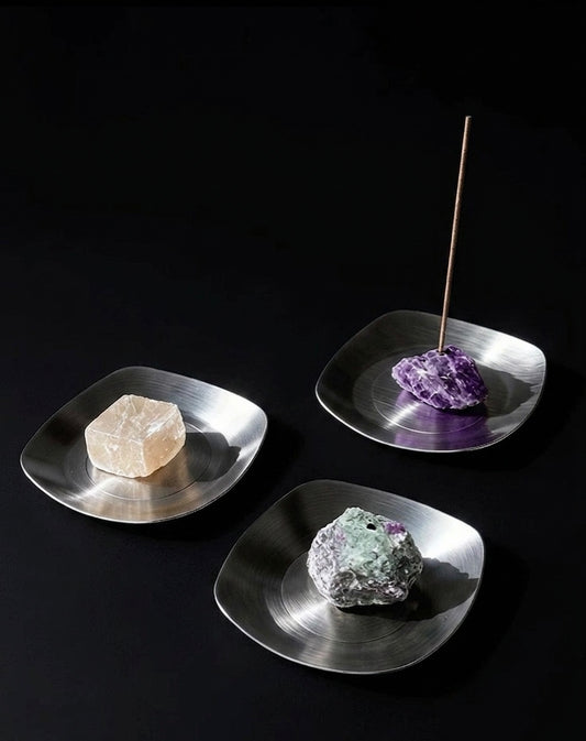 Three metallic incense holders with crystals on a black background