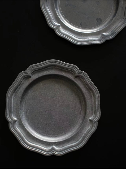 Two gray ceramic plates with decorative edges on a black background
