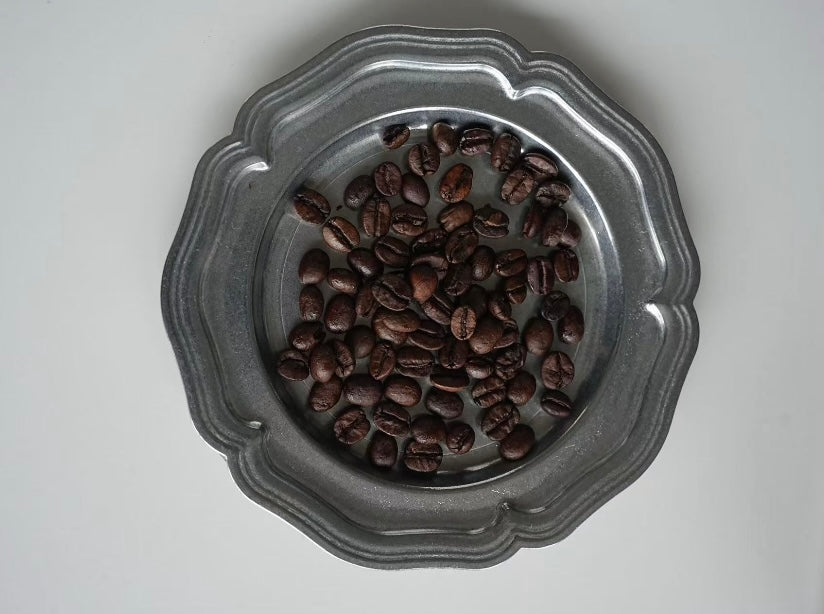 Roasted coffee beans in a decorative metal bowl on a light gray background
